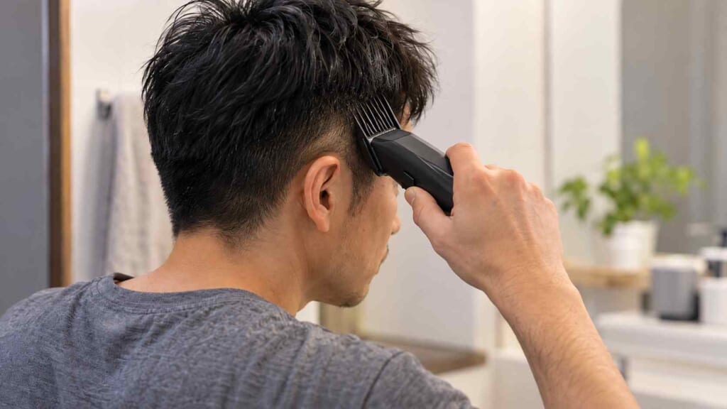 40代の日本人男性が自宅で電動バリカンを使い髪のサイドを刈り上げる様子